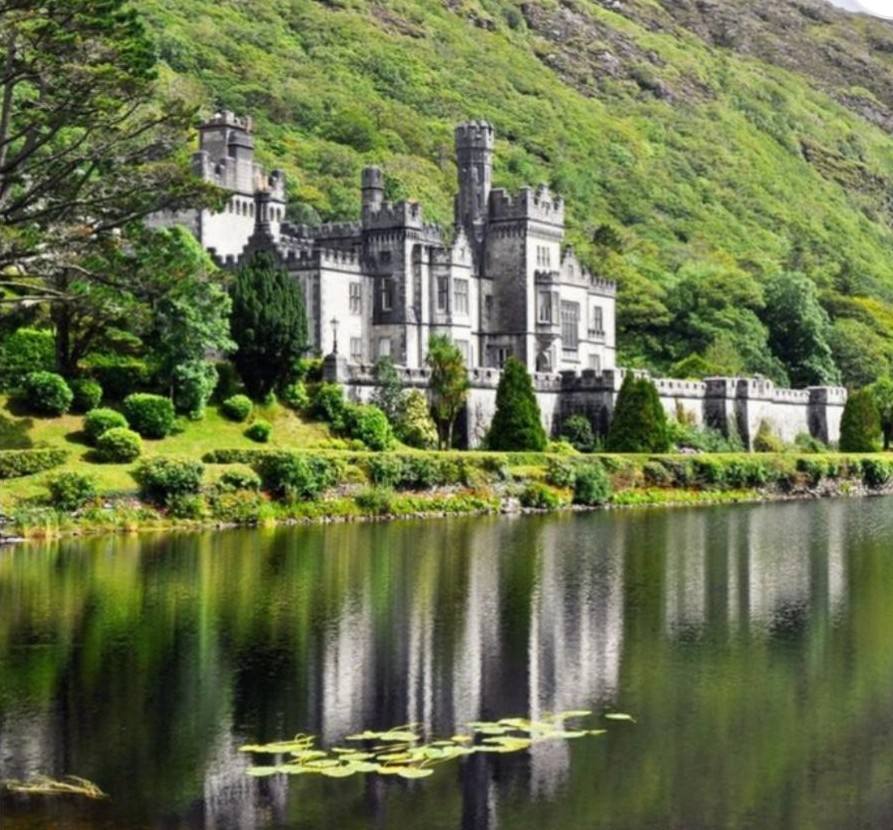 Kylemore Abbey in bright sunshine, reflected in the lough beneath its green mountainside, Connemara