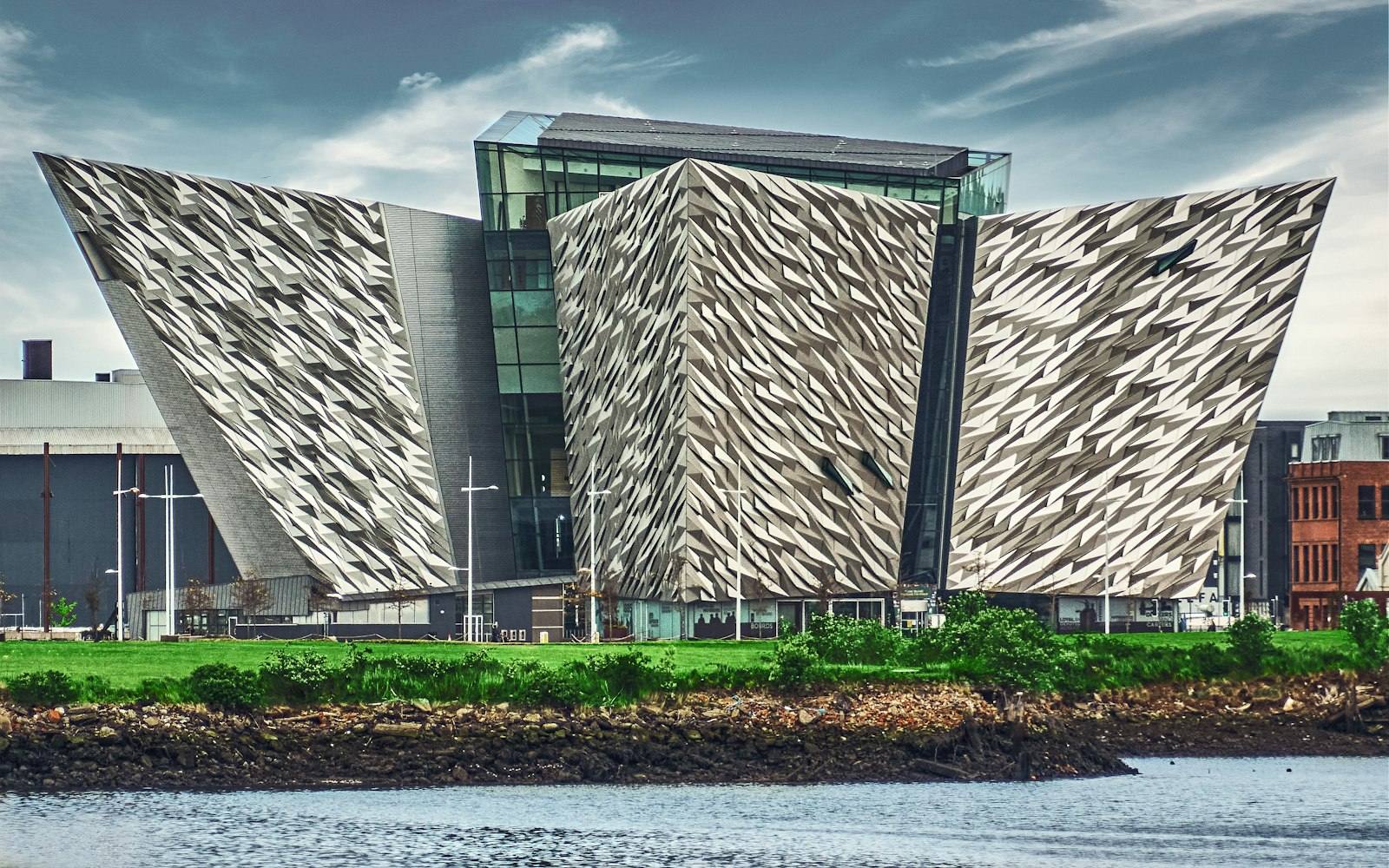 The angular silver hull-shaped facades of Titanic Belfast rising above the water of the Titanic Quarter